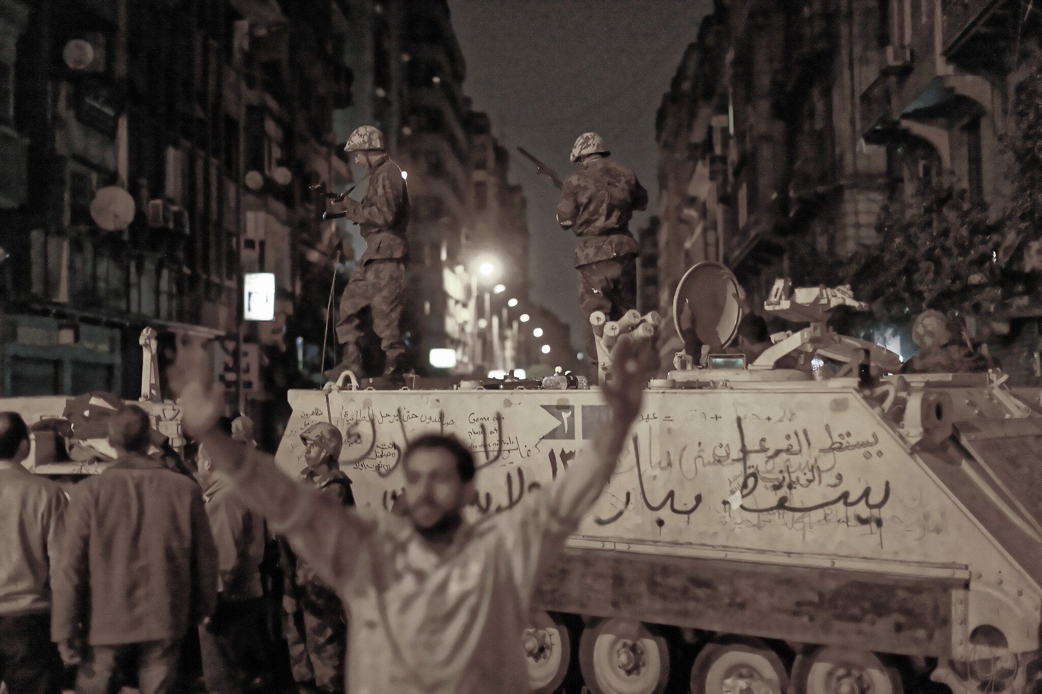A protest leader signals to demonstrators against the backdrop of armored army vehicles and soldiers blocking one of the entrances into Tahrir Square. The Army's role remained ambiguous: it was often unclear whether it was there more to protect protesters or monitor proceedings.