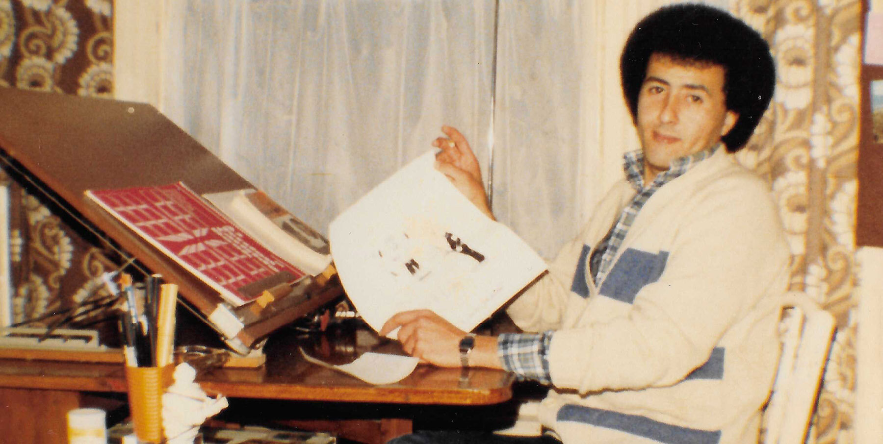 Hasan "Alsatoor" Dhaimish en su mesa de dibujo en Burnley, hacia 1980 (cortesía de Sherif Dhaimish).