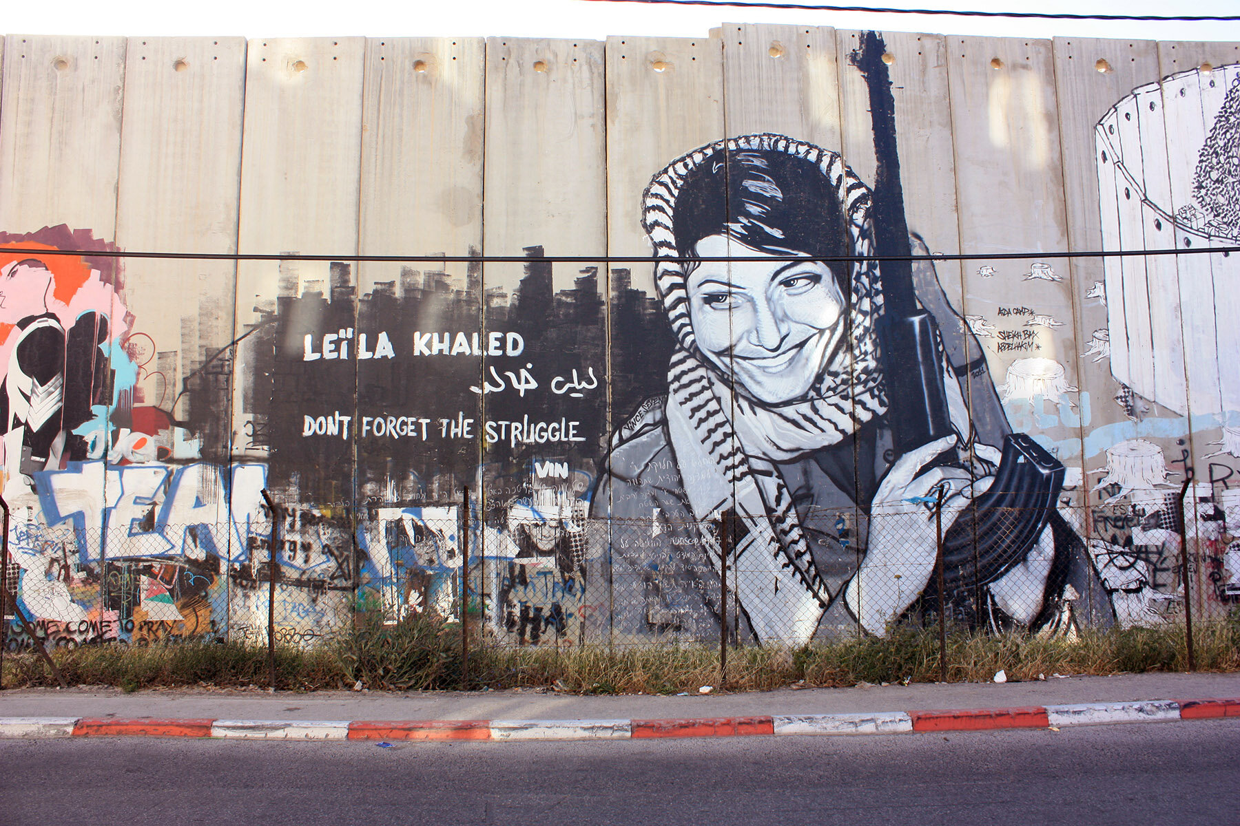 A mural of  Leila Khaled , the first woman member of the Popular Front for the Liberation of Palestine. The photograph of her in a kaffiyeh holding an AK-47 rifle, taken by Eddie Adams, became a symbol of the Palestinian resistance in the 1970s. She was also the first woman to hijack a plane in the late 1960s, and has consequently gone down in history as both a hero and a terrorist. Her mural on the wall, near Bethlehem in the West Bank, is a staunch reminder of both the resistance's past and its contested presence.