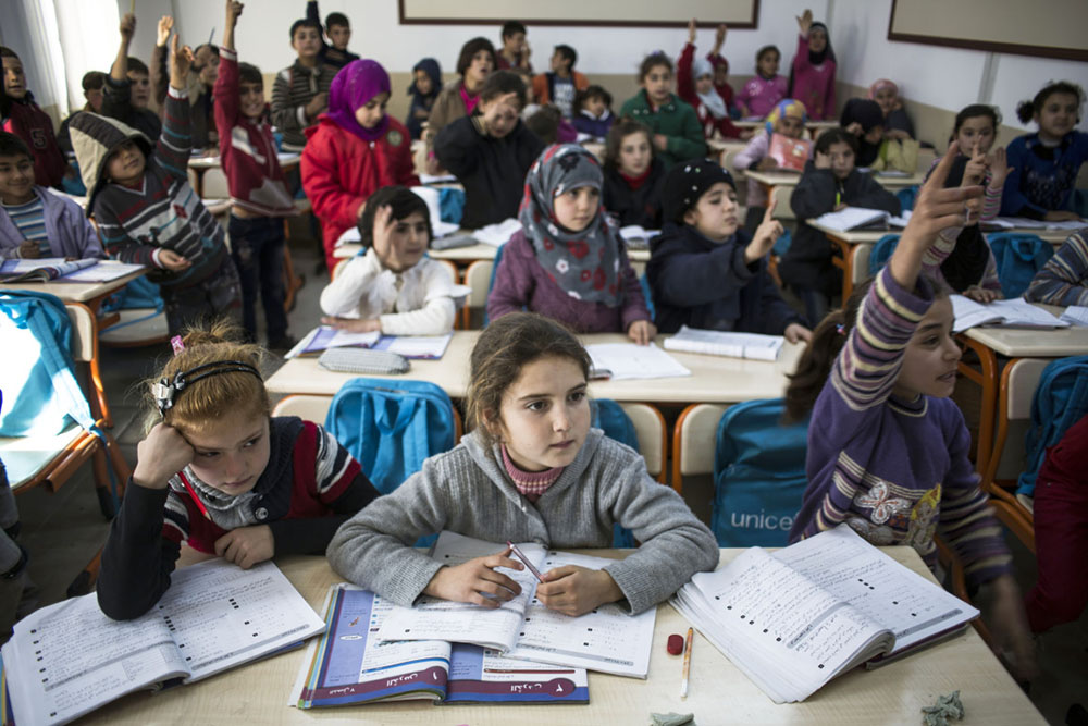 Pupils hold up their hands to catch the teacher’s attention at a Unicef school in the Eslahiye refugee camp in southern Turkey (Athanasiadis)