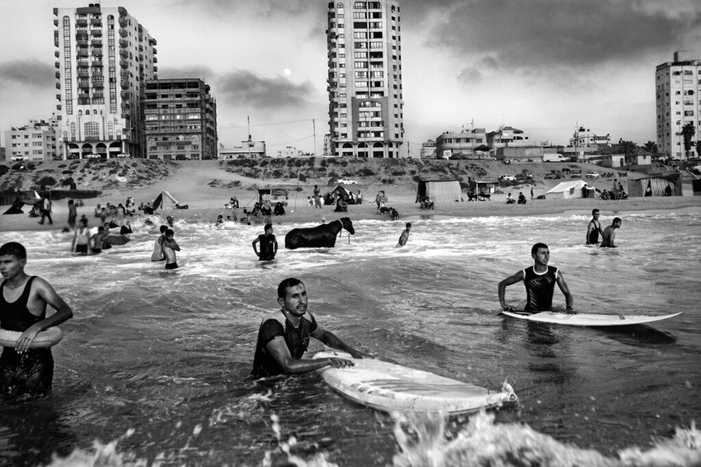 Still from the "Gaza Surf Club" from directors Philip Gnadt, Mickey Yamine, 2017, screening in AFMI's Palestinian Voices series, Nov. 2023. Amer Aldos (17) and Asam Abu Assi (33) enter the sea from Gaza City, as a horse stands in the water near the shore.