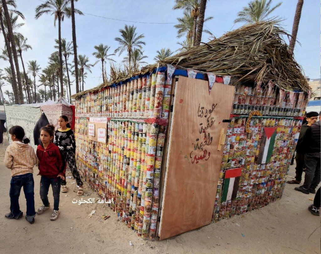 Tent made of tin cans in refugee camp in Deir Al Balah, accommodating displaced Gazans from Gaza City. Arabic on wooden door reads: ”Our return is inevitable, and the tent is an illusion.” Photo by Osama Kahlout, 2024,