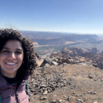 The author stands atop an extinct volcano, with a view to a valley carved into layered lava flows. Alula, north western Saudi Arabia.