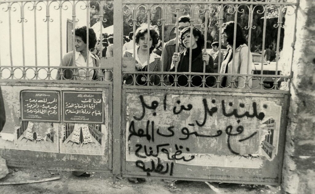 A group of students stand behind the college gate at the Faculty of Law in Beirut, the right half of which is tagged: “Let us fight to raise the level of education,” signed, “The Organization for Student Struggle.”